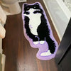 A plush rug shaped like a black and white cat with purple accents, used as a non-slip mat.