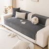 A gray non-slip sofa cover with a quilted texture and white accents displayed on a white sofa.