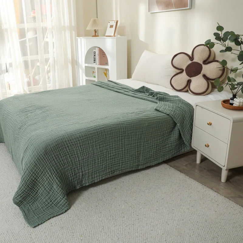 A light green quilted blanket draped over a white bed, next to a white nightstand with decorative items.