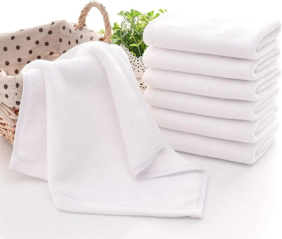 A stack of ten white cotton face towels is shown next to a folded towel on a white surface.