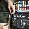 A hand is shown holding a black sewing kit containing various threads, needles, and tools for crafting.