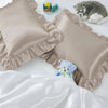 Two ruffled satin pillowcases in beige and white with silky envelope closures shown on a white surface.
