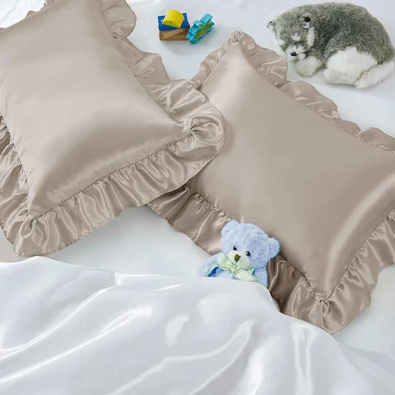 Two ruffled satin pillowcases in beige and white with silky envelope closures shown on a white surface.