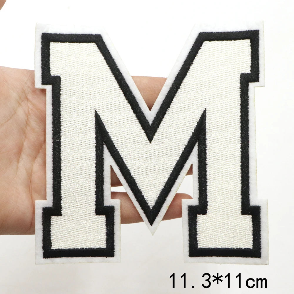 A hand holds a large letter M patch with black outline and white fabric on a white background.