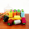 A collection of various colored sewing threads on a wooden surface, including spools and a glass jar.