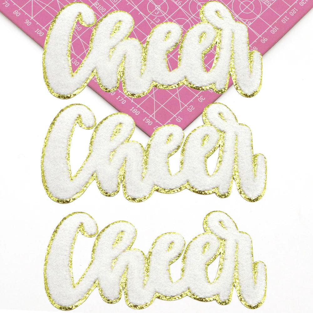 Three white embroidered cheer letters in gold glitter on a pink grid background