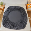 A dark gray fitted sheet is laid out on a white bed, showing its gathered texture.