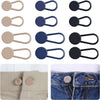 A set of metal waistbands with elastic extenders in various colors and finishes shown on denim fabric.