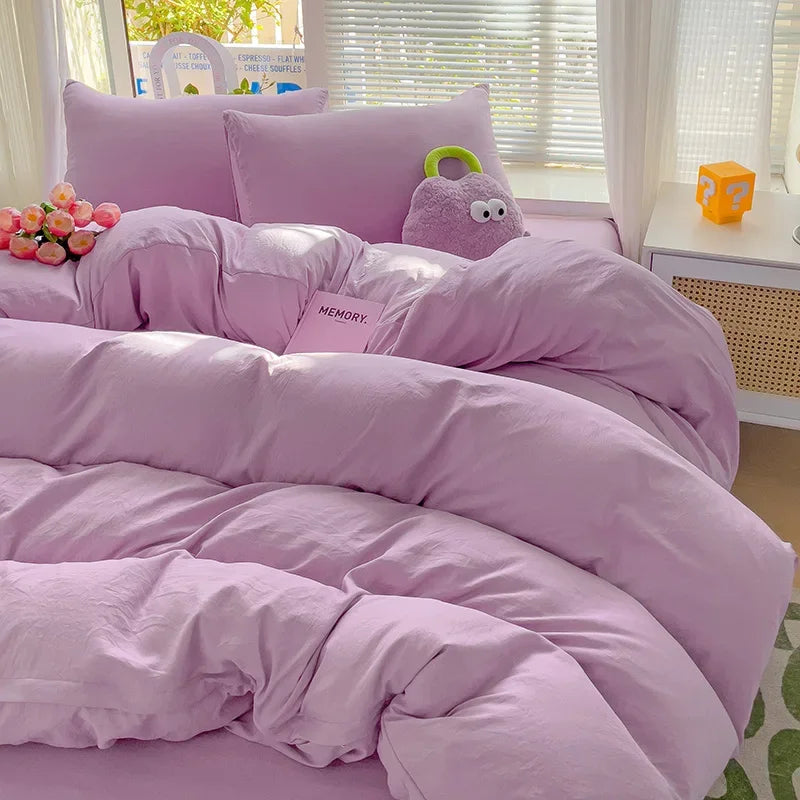 A purple cotton bed linen set featuring a duvet, pillows, and a stuffed elephant toy.
