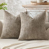 A pair of textured, olive green chenille pillows resting on a light-colored sofa with a cream blanket nearby.