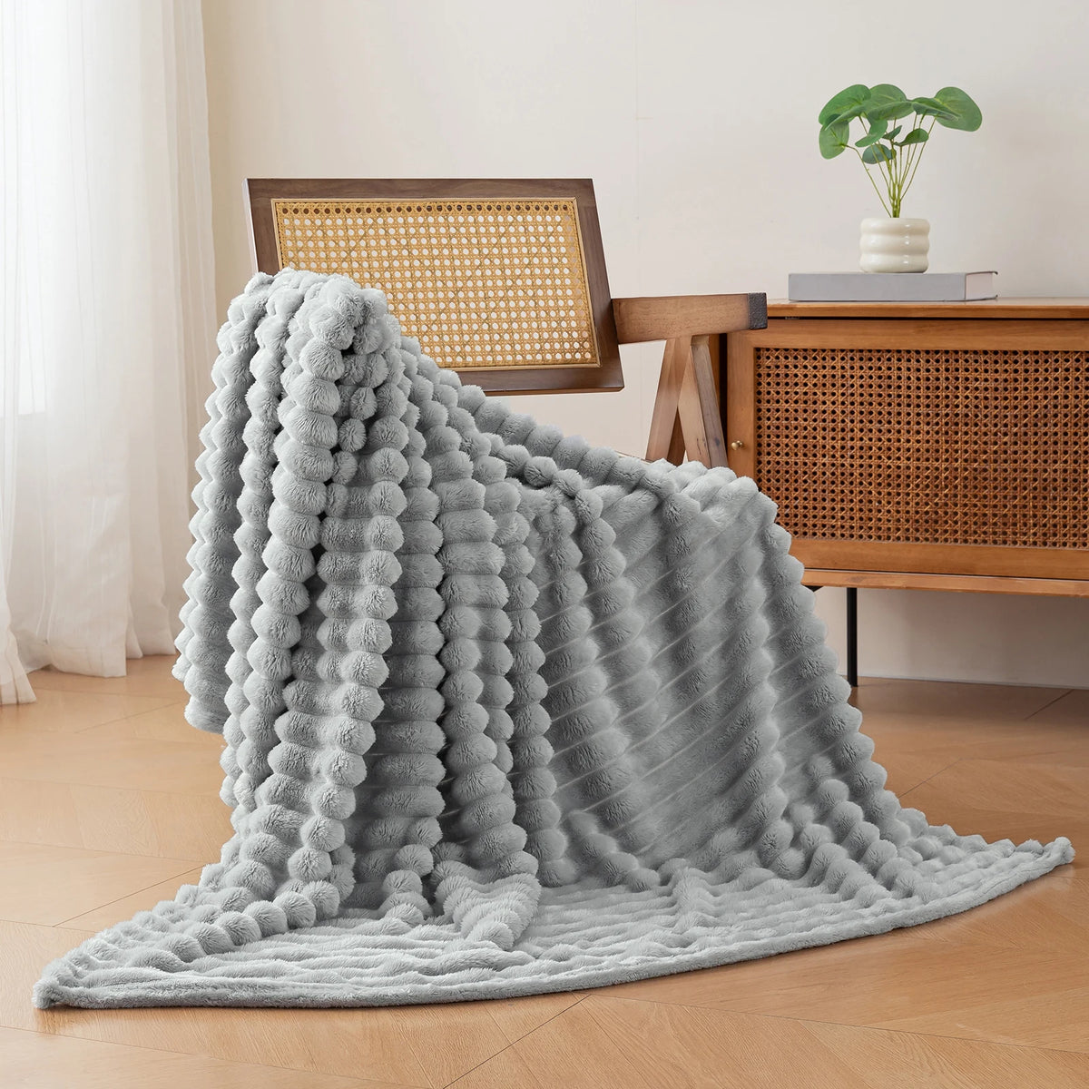 A soft gray flannel throw blanket draped on a wooden surface next to a desk and potted plant.