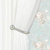 A silver metal curtain holdback hook is visible on a white pleated curtain against a light floral wallpaper.