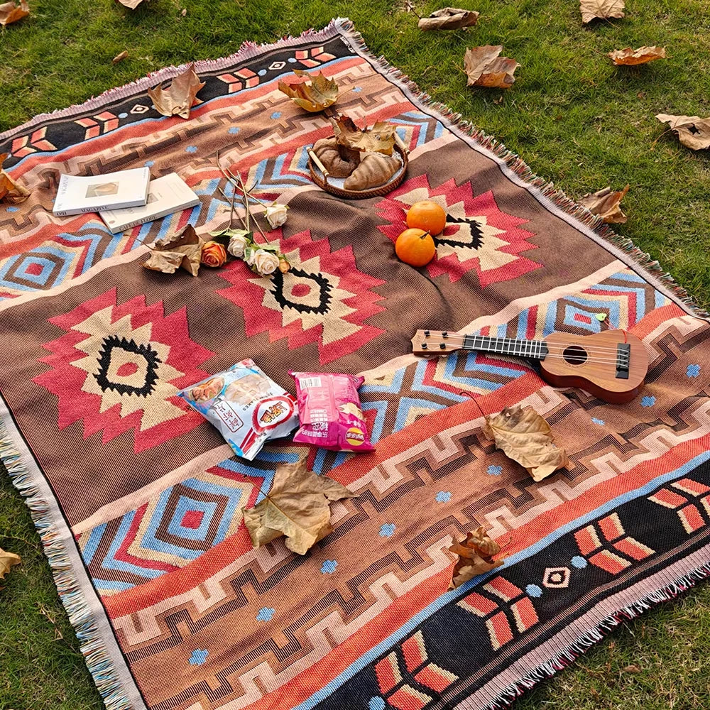 A brown and rust-colored knitted blanket with geometric patterns laid out on green grass.