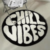 A round black rug with white text that reads CHILL VIBES is displayed under a metal stand.