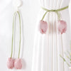 Pink tulip flower curtain tie backs with green fabric ties hanging on a white curtain.