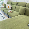 A sectional sofa covered in olive green jacquard stretch fabric with light cream accent pillows.