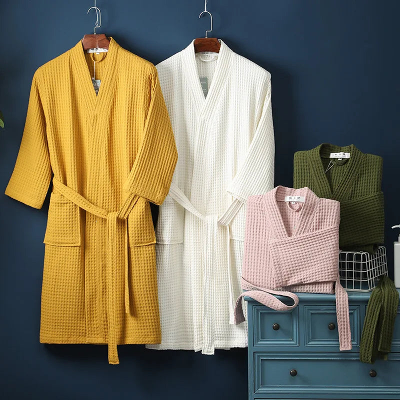 A yellow cotton terry robe and a white cotton terry robe hanging against a dark blue wall.