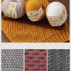 Three balls of wool thread in beige, yellow, and white are displayed on a wooden board.