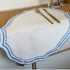 A white cotton linen placemat with blue embroidery and two gold-toned forks resting on it.