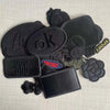 A set of five black embroidered leather patches with self-adhesive backing, including letters, symbols, and words like OK and
