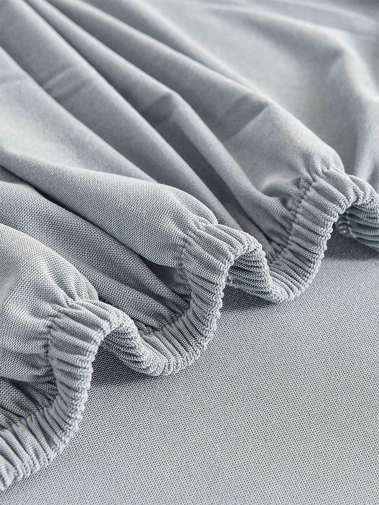 Light gray elastic sofa slipcovers folded and draped on a surface.