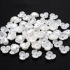 A collection of small, white imitation pearl flower spacer beads scattered on a black surface.