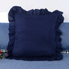 A dark navy blue ruffled pillow cover displayed on a blue fabric surface.