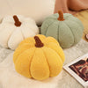 Three plush pumpkin throw pillows in white, green, and yellow with brown stems resting on a light textured surface.