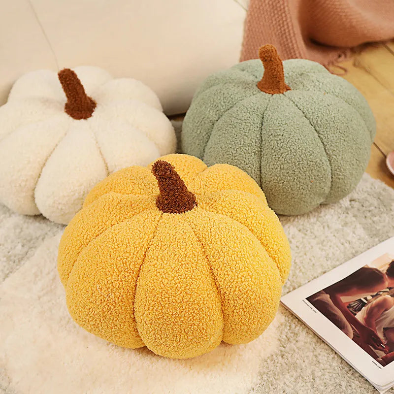 Three plush pumpkin throw pillows in white, green, and yellow with brown stems resting on a light textured surface.