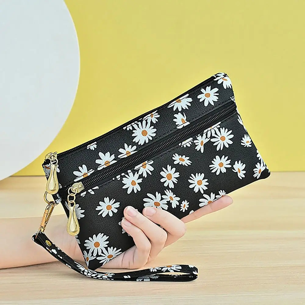 A black PU leather coin purse with a floral pattern and gold hardware is held by a hand against a yellow background.