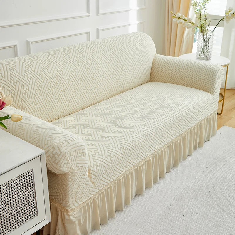 A beige jacquard stretch sofa cover featuring a geometric pattern and a ruffled hem.
