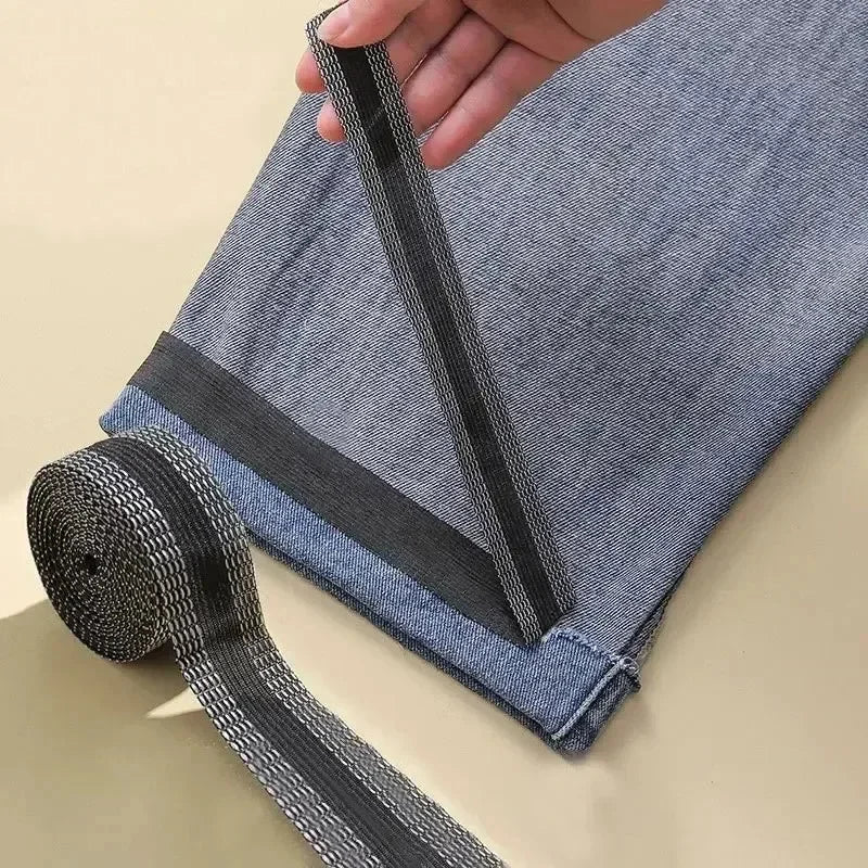 A hand is pulling out black iron-on hem tape from the cuff of a denim pant leg.