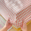 Hands are holding a pink and white checkered flannel fitted sheet with deep pockets.