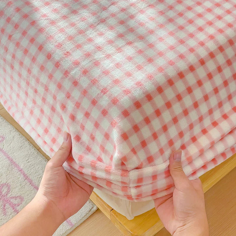 Hands are holding a pink and white checkered flannel fitted sheet with deep pockets.