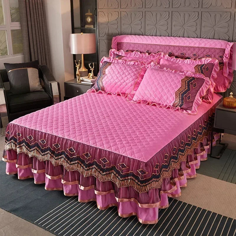 A pink quilted bed skirt with purple embroidery and ruffled edges is displayed on a bed.