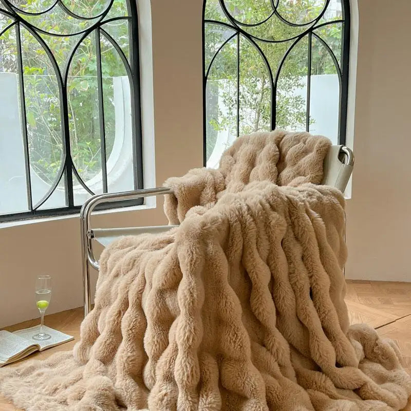 A plush faux fur throw blanket in a beige color draped over a metal chair near a window.