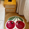 A round, organic-shaped rug in shades of red and green with a white border lies on a light wooden floor.