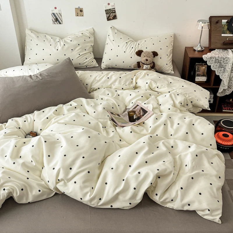 A white duvet cover set with a black polka dot pattern is displayed on a bed, surrounded by pillows and a teddy bear.