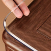 A hand is holding a clear PVC table protector mat with a dark brown border over a wooden surface.