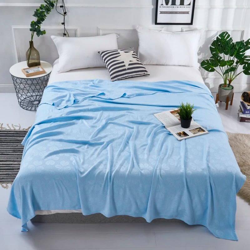 A light blue bamboo fiber cooling blanket is spread on a white bed with white pillows and decorative accents.