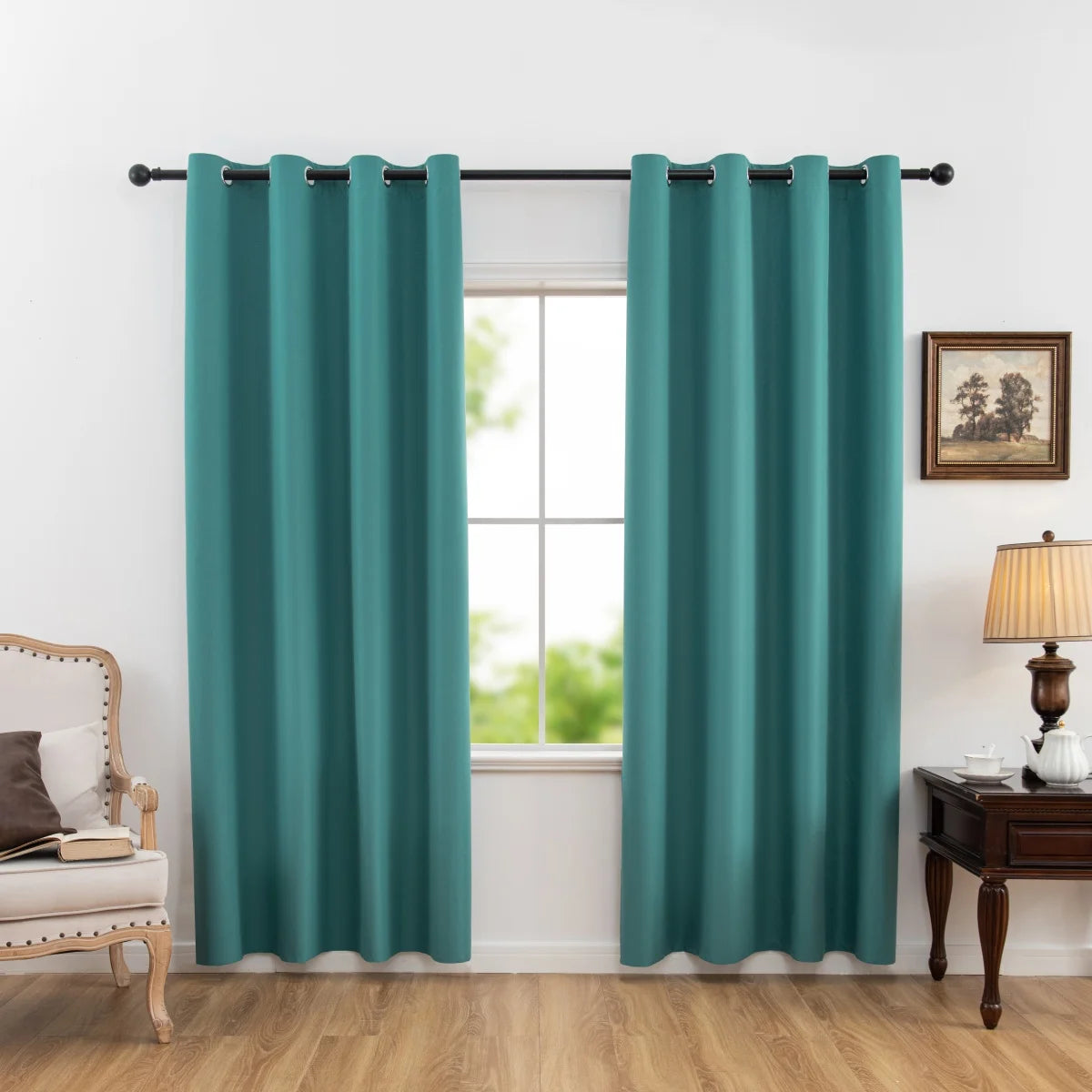 A pair of teal blackout curtains hanging in a window frame with a wooden dresser and chair nearby.