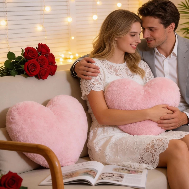 A young woman is holding a pink heart-shaped plush cushion while sitting on a sofa.