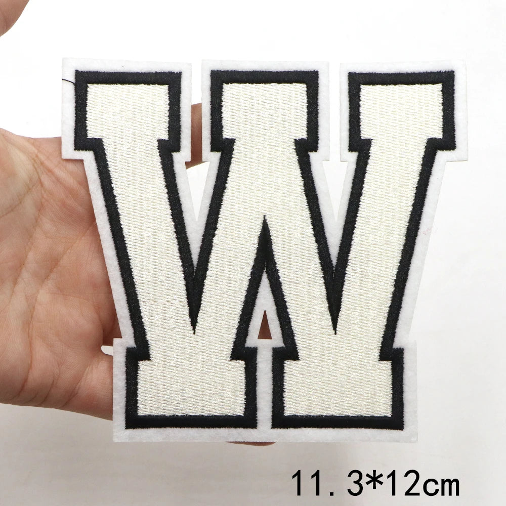 A hand holds a white letter W patch with black outline and stitching on a white background.