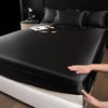 A hand is adjusting a black satin fitted sheet over a mattress.
