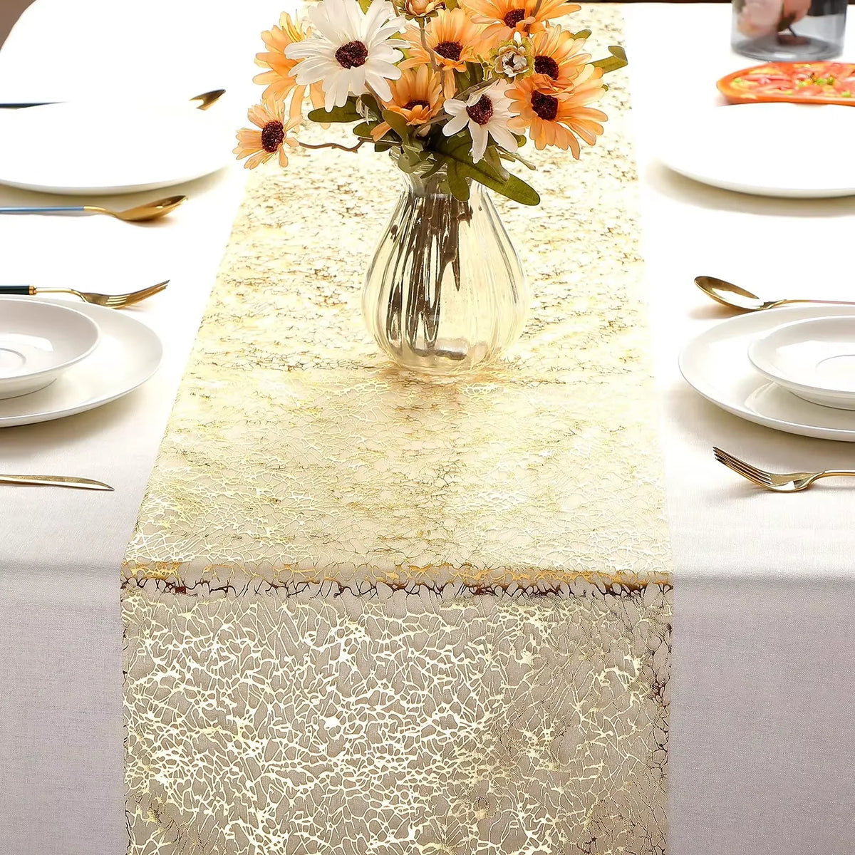Metallic gold table runner set on a white tablecloth with floral centerpiece and place settings