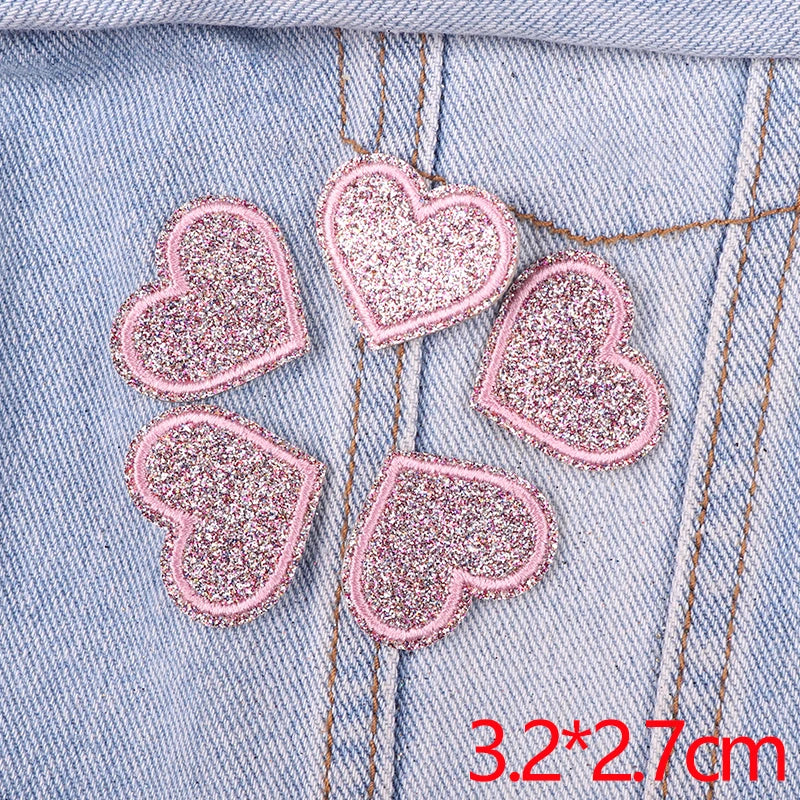 Five pink glitter heart patches are placed on a light blue denim fabric.