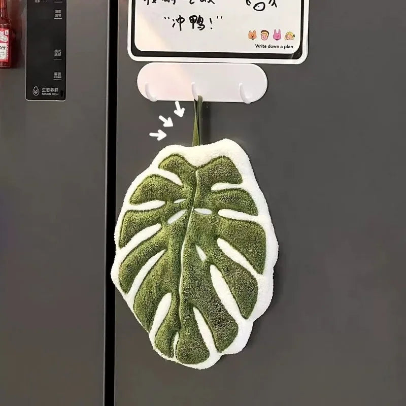 A green and white embroidered leaf hand towel hanging on a door