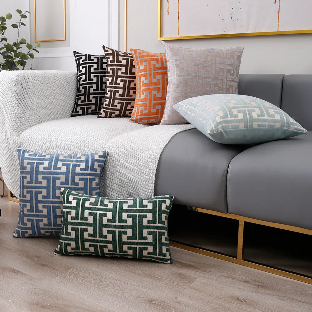 A collection of geometric jacquard lumbar pillow covers in shades of gray, orange, and teal displayed on a sofa.