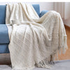A cream colored oversized knitted tassel throw blanket draped over a blue sofa.