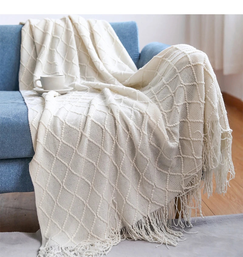 A cream colored oversized knitted tassel throw blanket draped over a blue sofa.